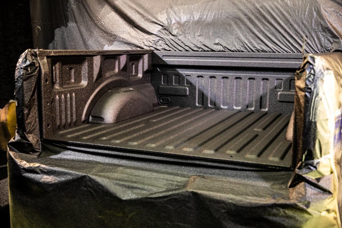 A pickup truck bed coated in black spray-on bedliner, covered in black masking material in a garage.