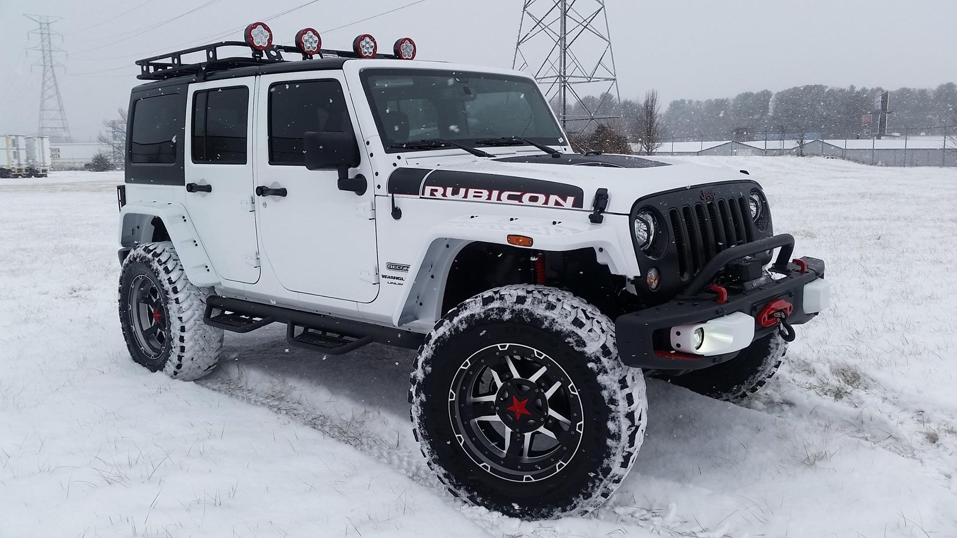 White Jeep Rubicon with black accents, roof rack, and large tires in a snowy landscape.