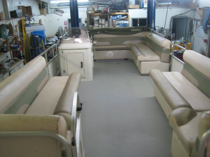 Interior view of a pontoon boat with beige and green seating in a workshop setting.