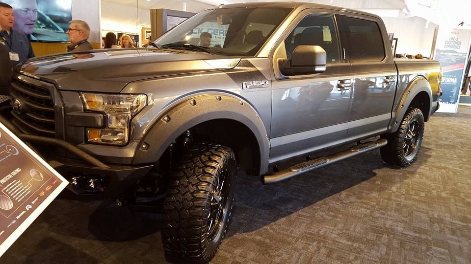 Gray Ford F-150 pickup truck with black fender flares and large tires, displayed indoors at an auto show.
