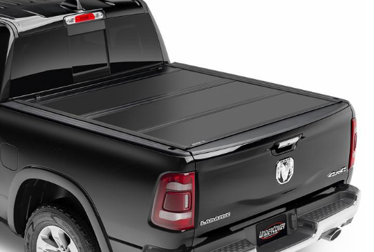 Black pickup truck with a closed, folding tonneau cover. The Ram truck has a silver bumper and a red taillight.