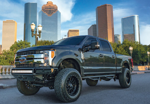 Dark gray lifted pickup truck parked on a road, city skyline in the background.