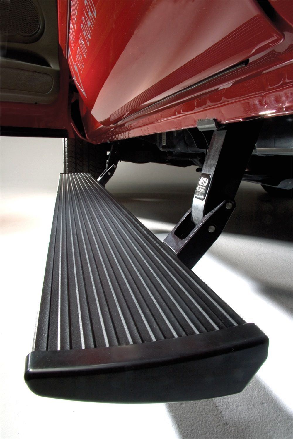 Black running board extended from a red truck. It features a textured surface and is angled slightly downward.