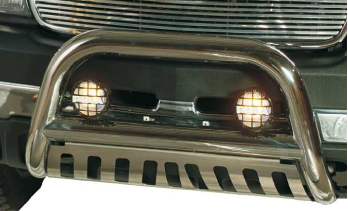 Close-up of a silver bull bar on a truck. The bull bar has two round, grid-covered lights illuminated in the center. 
