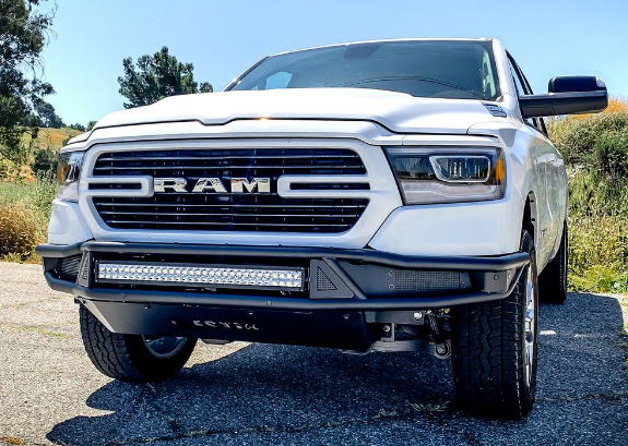 White Ram truck with a black aftermarket bumper and a light bar, parked on a paved road.