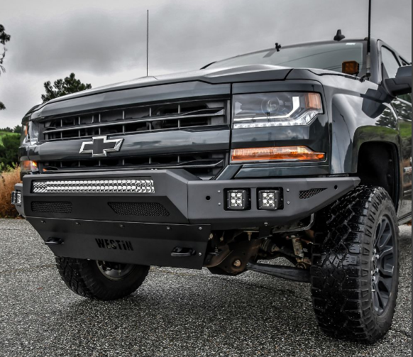 Black Chevrolet Silverado truck with an aftermarket front bumper featuring LED lights, parked on pavement.