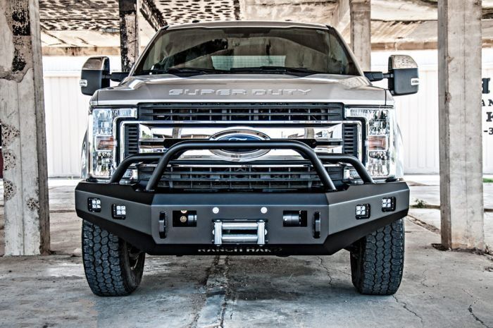 Silver Ford Super Duty truck with a heavy-duty black bumper, winch, and lights, parked in front of a distressed building.