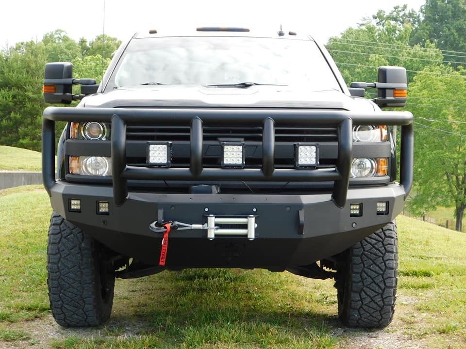 Black pickup truck with a heavy-duty bumper and grille guard, fitted with spotlights, and a winch, parked outside.