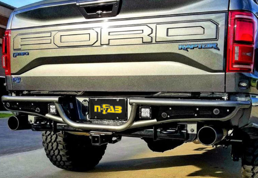 Rear view of a Ford F-150 Raptor with a custom N-FAB bumper and aftermarket exhaust. Silver truck with black tires.