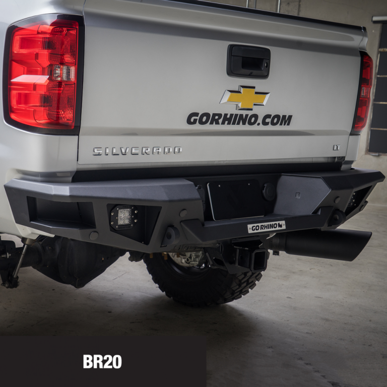A black, aftermarket rear bumper on a silver Chevrolet Silverado truck. The bumper has integrated lights and a hitch.