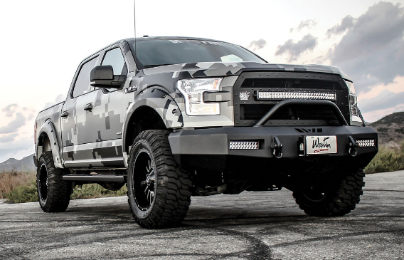 Camouflage-wrapped Ford F-150 truck with black off-road modifications, LED lights, and large tires, parked on asphalt.