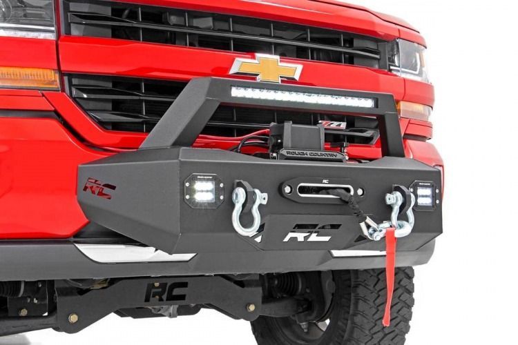 Red Chevrolet truck with a black aftermarket front bumper, winch, and LED light bar. The bumper has integrated fog lights and tow hooks.