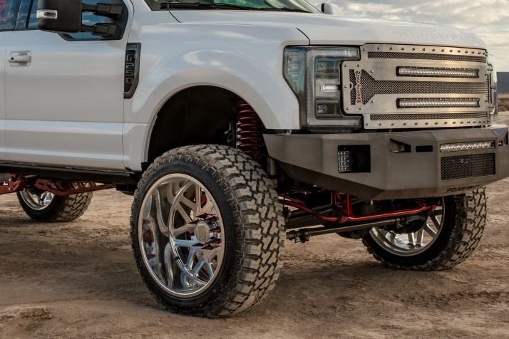 White lifted truck with large tires and a custom grill in a desert setting.