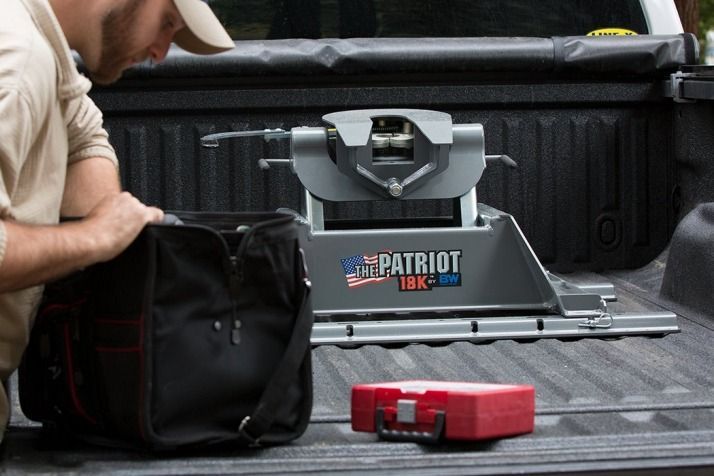 Man in a truck bed looks at a tool bag next to a fifth-wheel trailer hitch labeled 