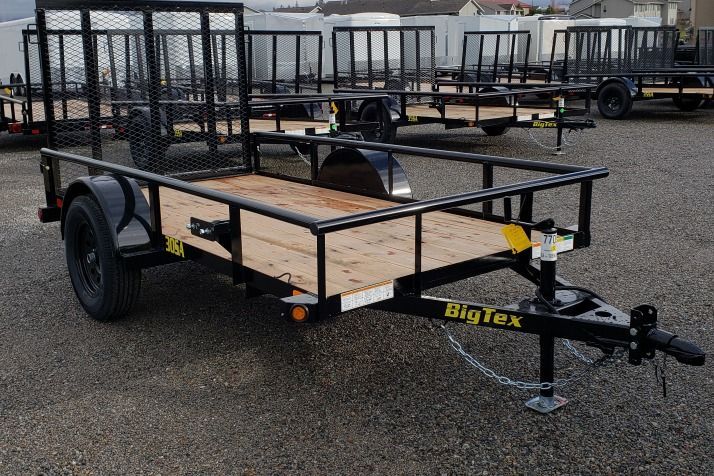 A black Big Tex utility trailer with a wooden deck and metal railings, parked outside on a concrete surface.