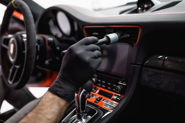 Gloved hand cleaning a car’s dashboard with a cloth near the center console