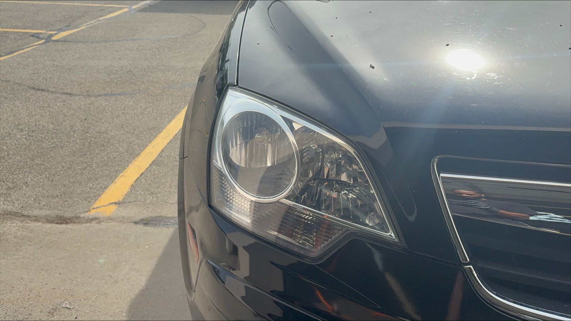 Close-up of the front left headlight and grille of a black car in a parking lot.