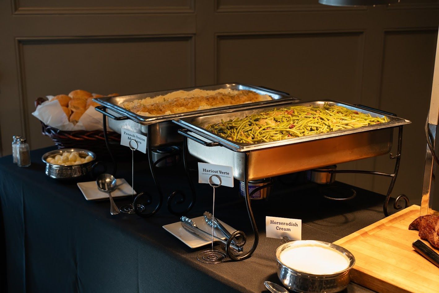 Buffet table with two stainless steel chafing dishes of food and serving utensils