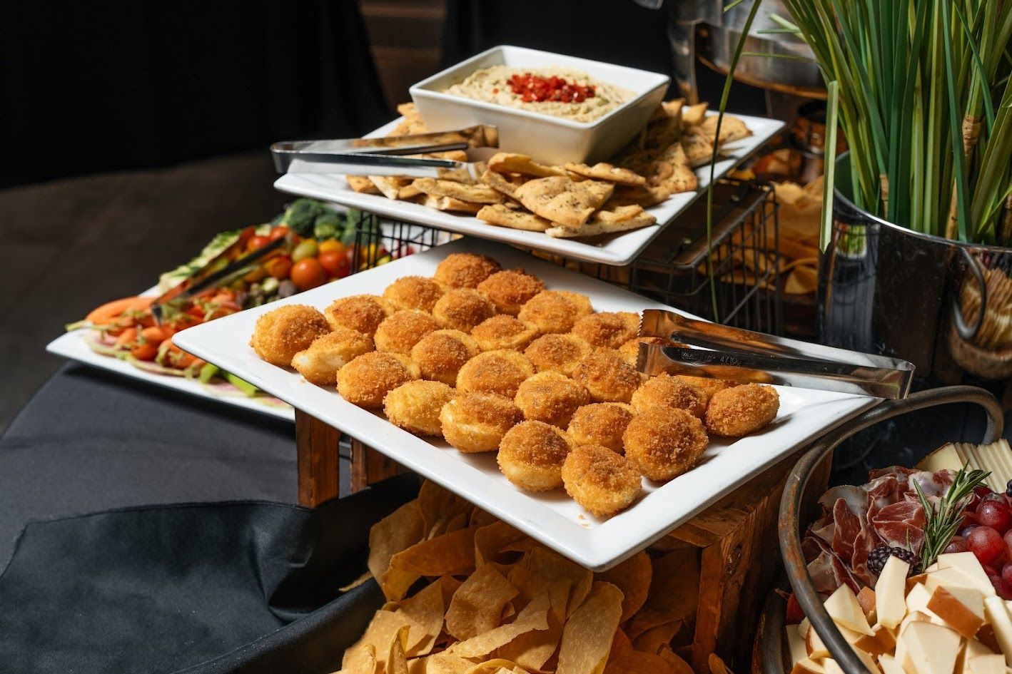 Buffet table with assorted appetizers and dips on white platters and black tablecloth.