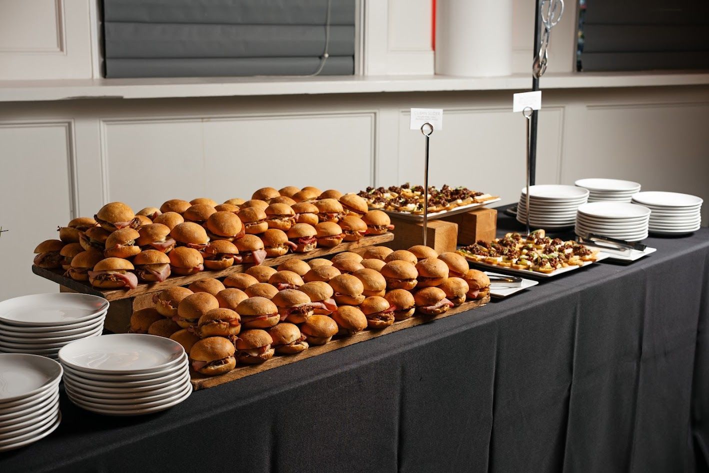 Buffet table with stacks of plates and trays of pastries and muffins under a window
