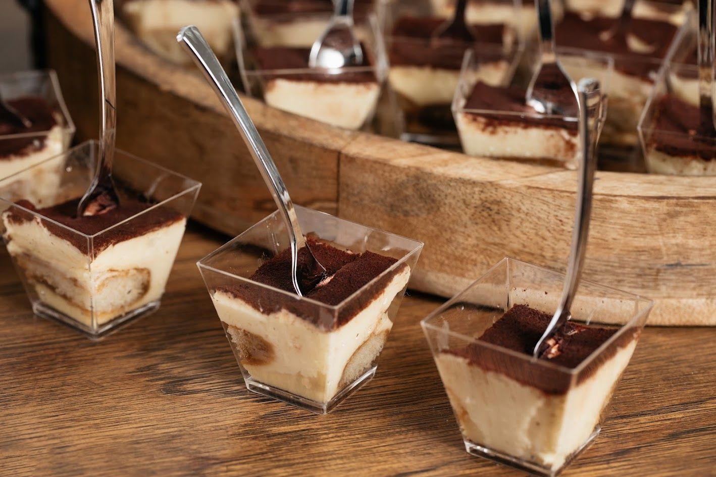 Chocolate mousse desserts in small square cups with spoons on a wooden tray