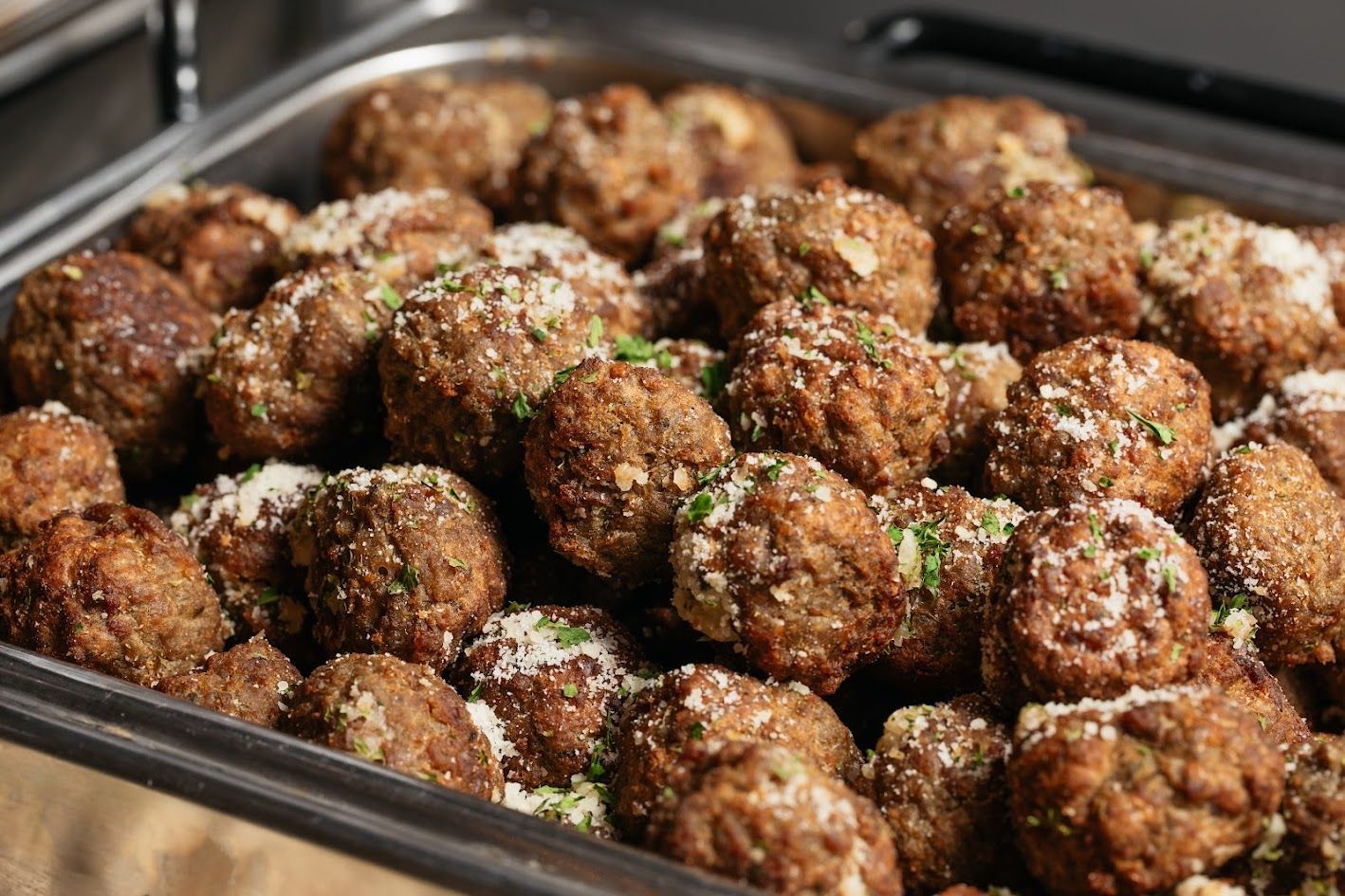 Tray of browned meatballs topped with grated cheese and herbs