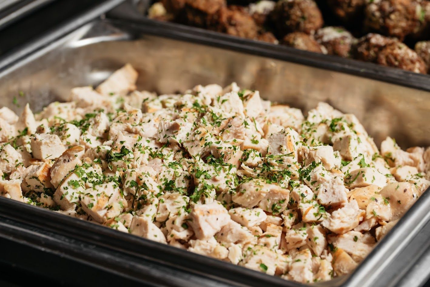 Tray of diced chicken seasoned with herbs in a buffet-style serving pan