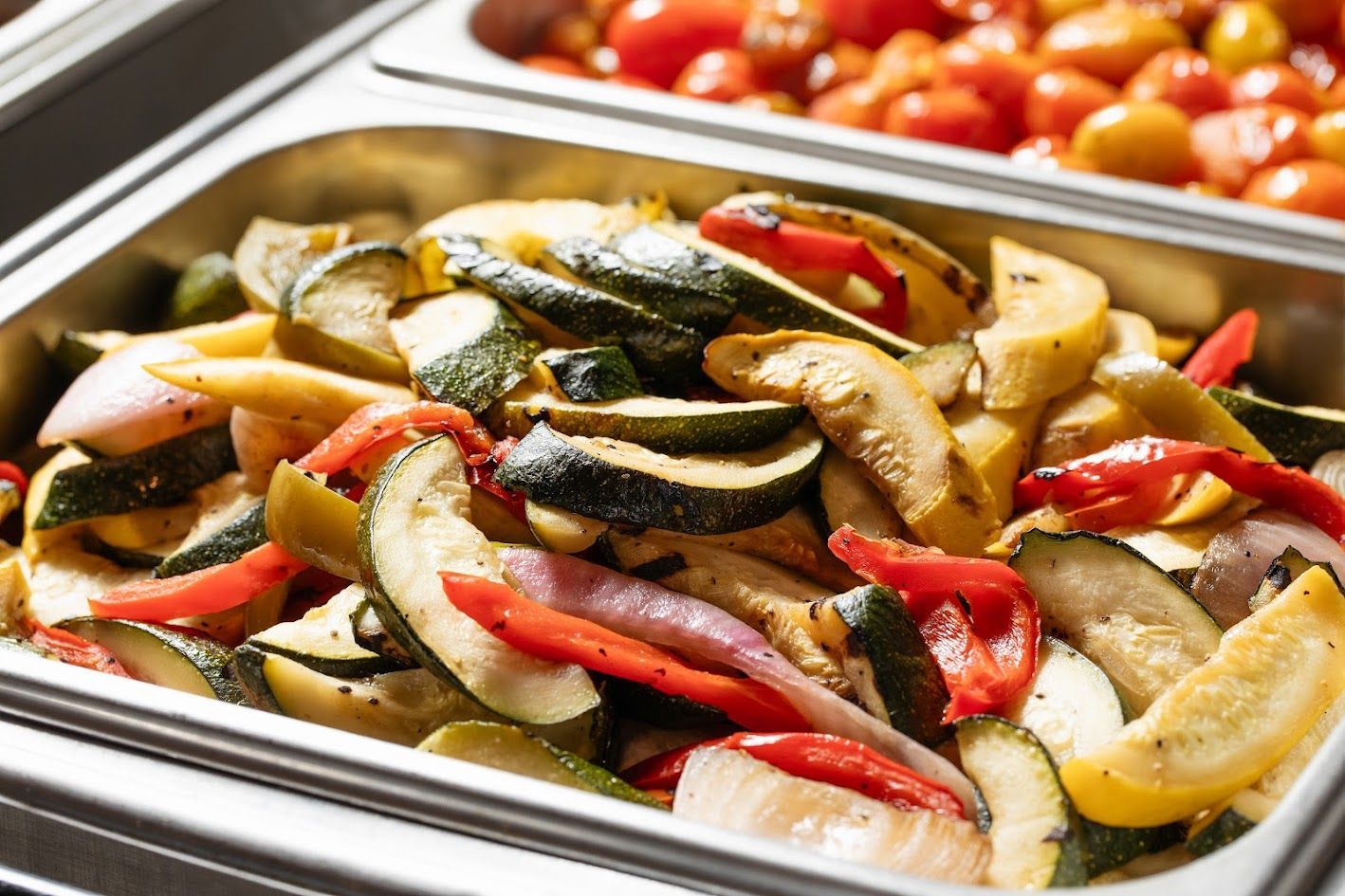 Tray of roasted vegetables with sliced zucchini, peppers, onions, and eggplant in a buffet pan