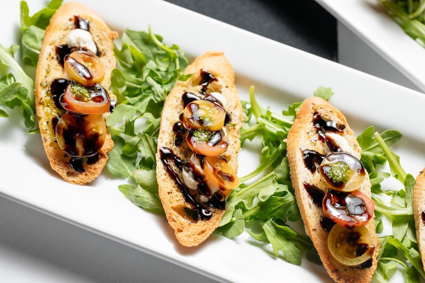Three toasted crostini topped with sliced vegetables on a bed of greens on a white platter