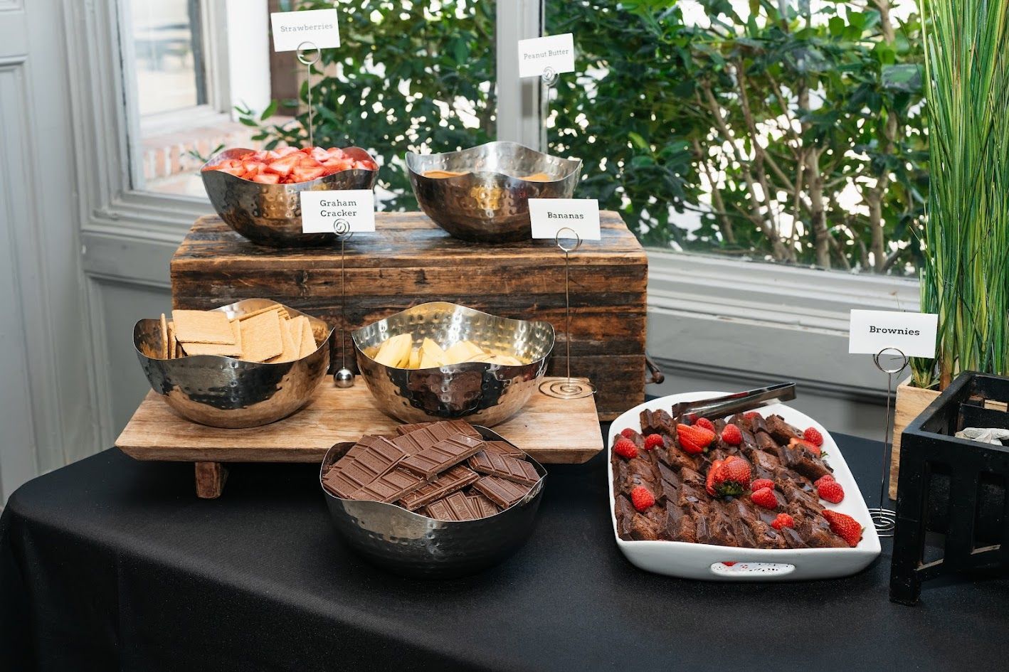 Dessert buffet with chocolate cakes and berry-topped dishes on a black table near a window