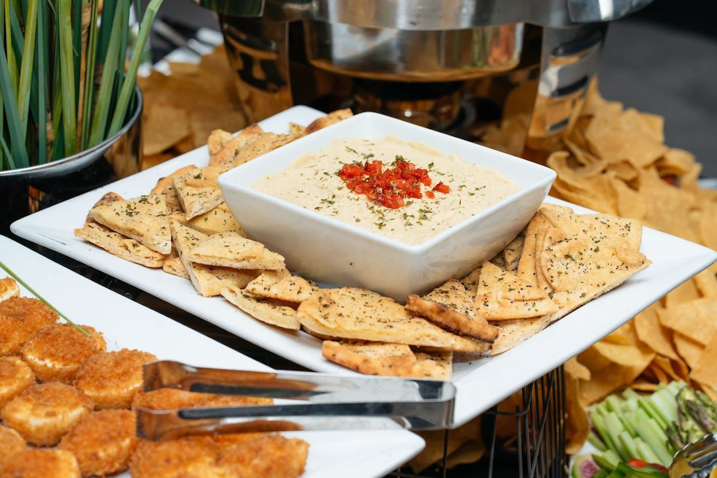 Square platter with crackers around a white dip bowl topped with red seasoning at a buffet table