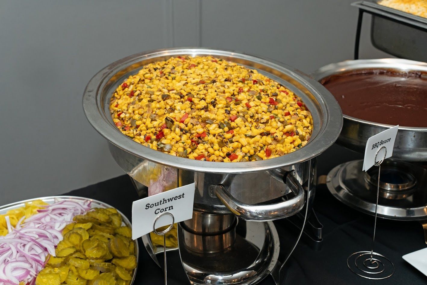 Buffet table with a large pan of yellow rice and vegetables beside sliced onions and sauces