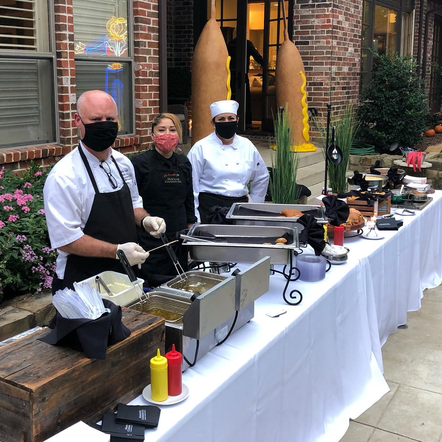 A man wearing a mask is standing in front of a long table filled with food.