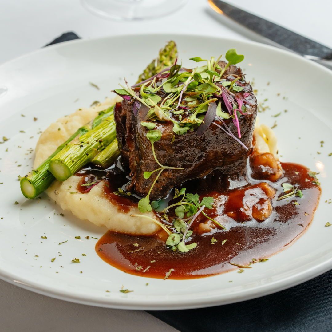 A white plate topped with a piece of meat mashed potatoes and asparagus.