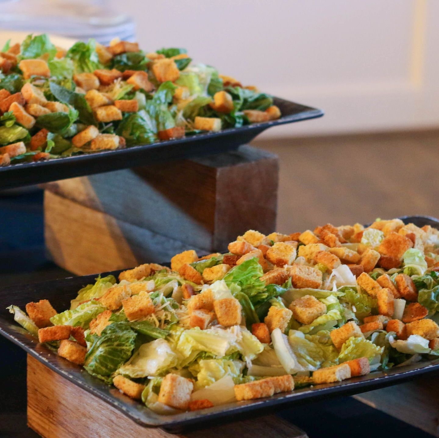 Two trays of salad with croutons and lettuce on a table.
