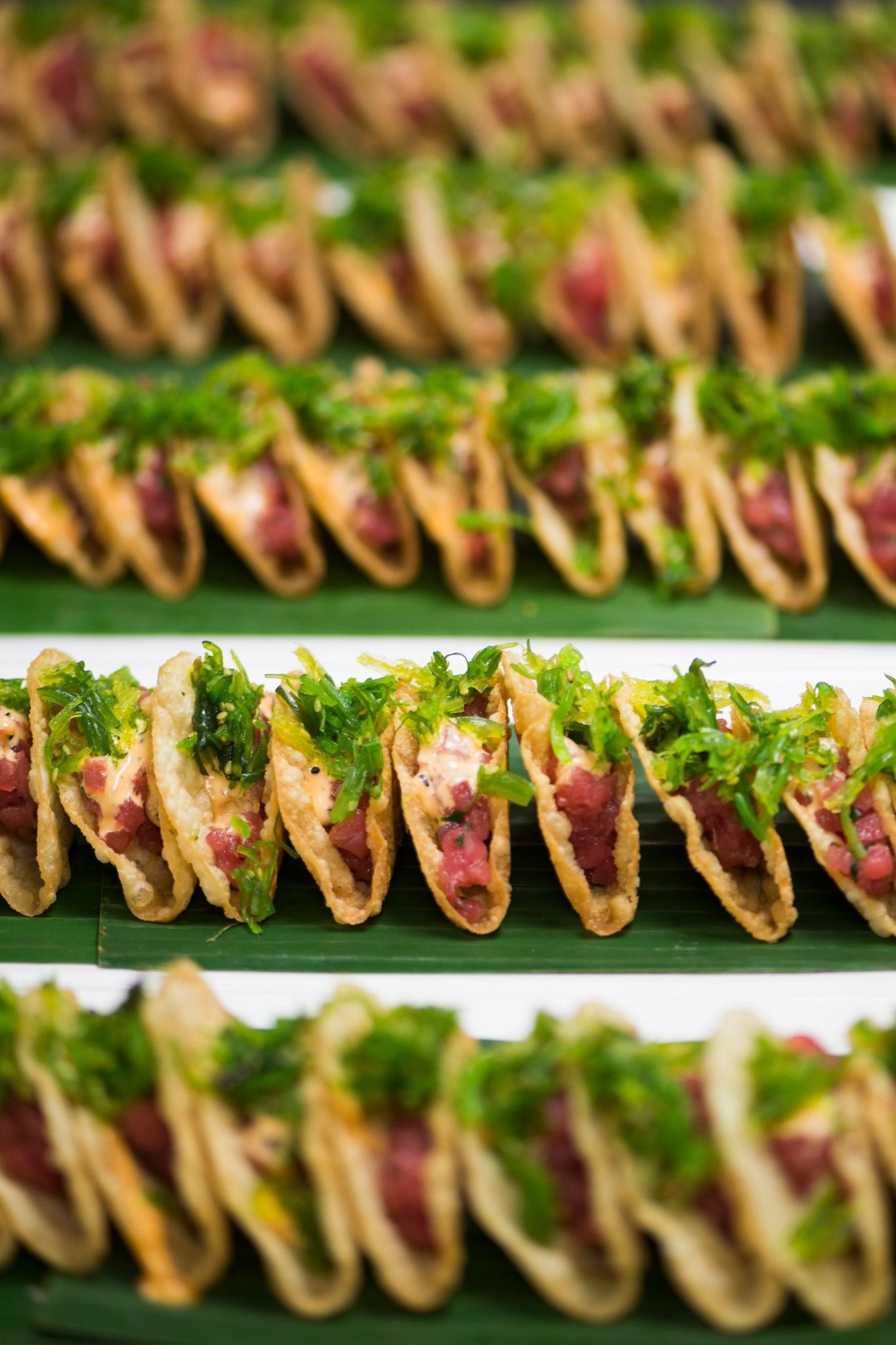 A row of tacos with meat and greens on a banana leaf.