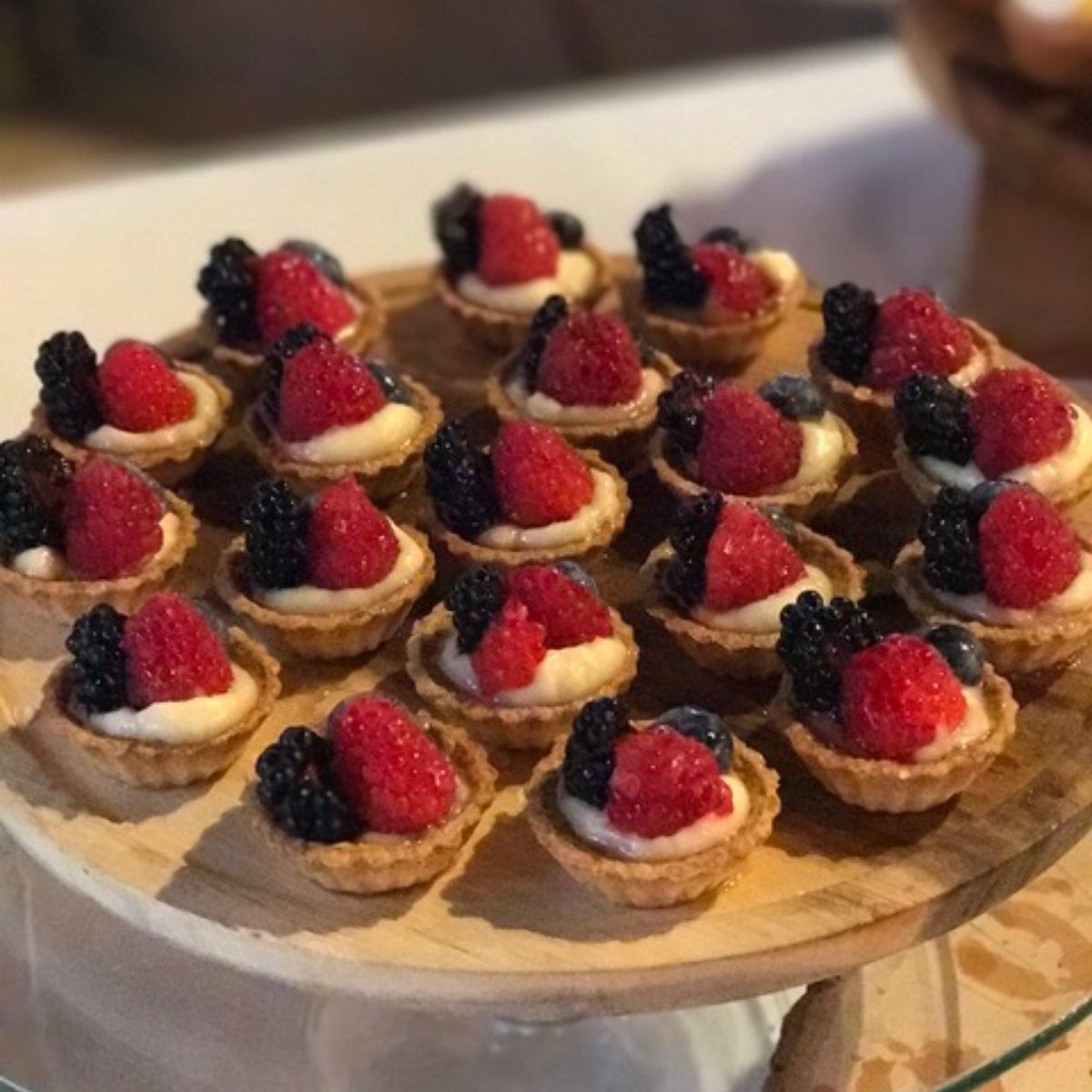 A wooden tray filled with small desserts with raspberries and blackberries on top.