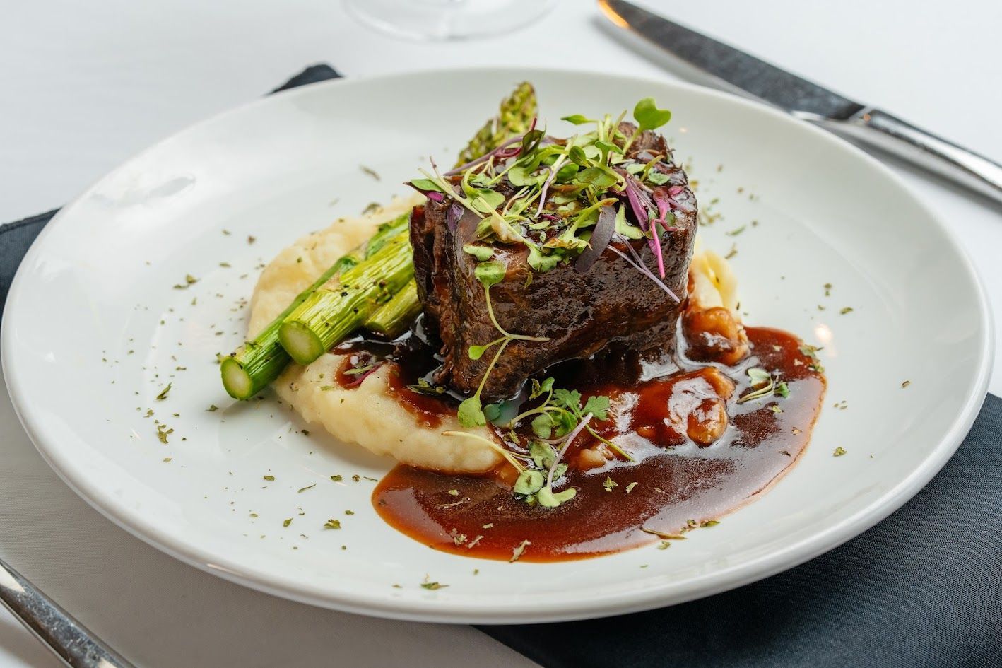 A white plate topped with a piece of meat, mashed potatoes, and asparagus.