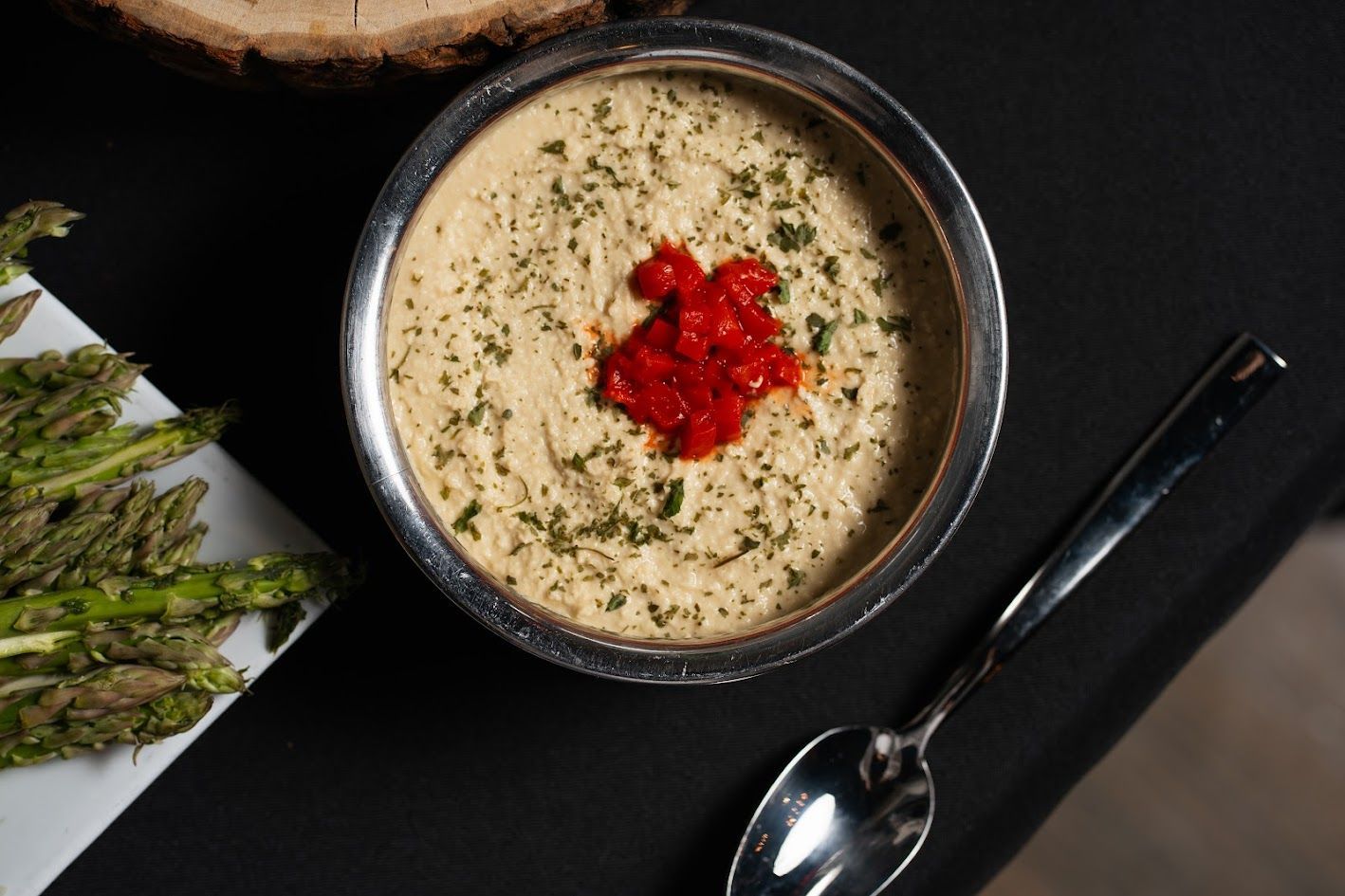 A bowl of soup with a spoon and asparagus on a table.