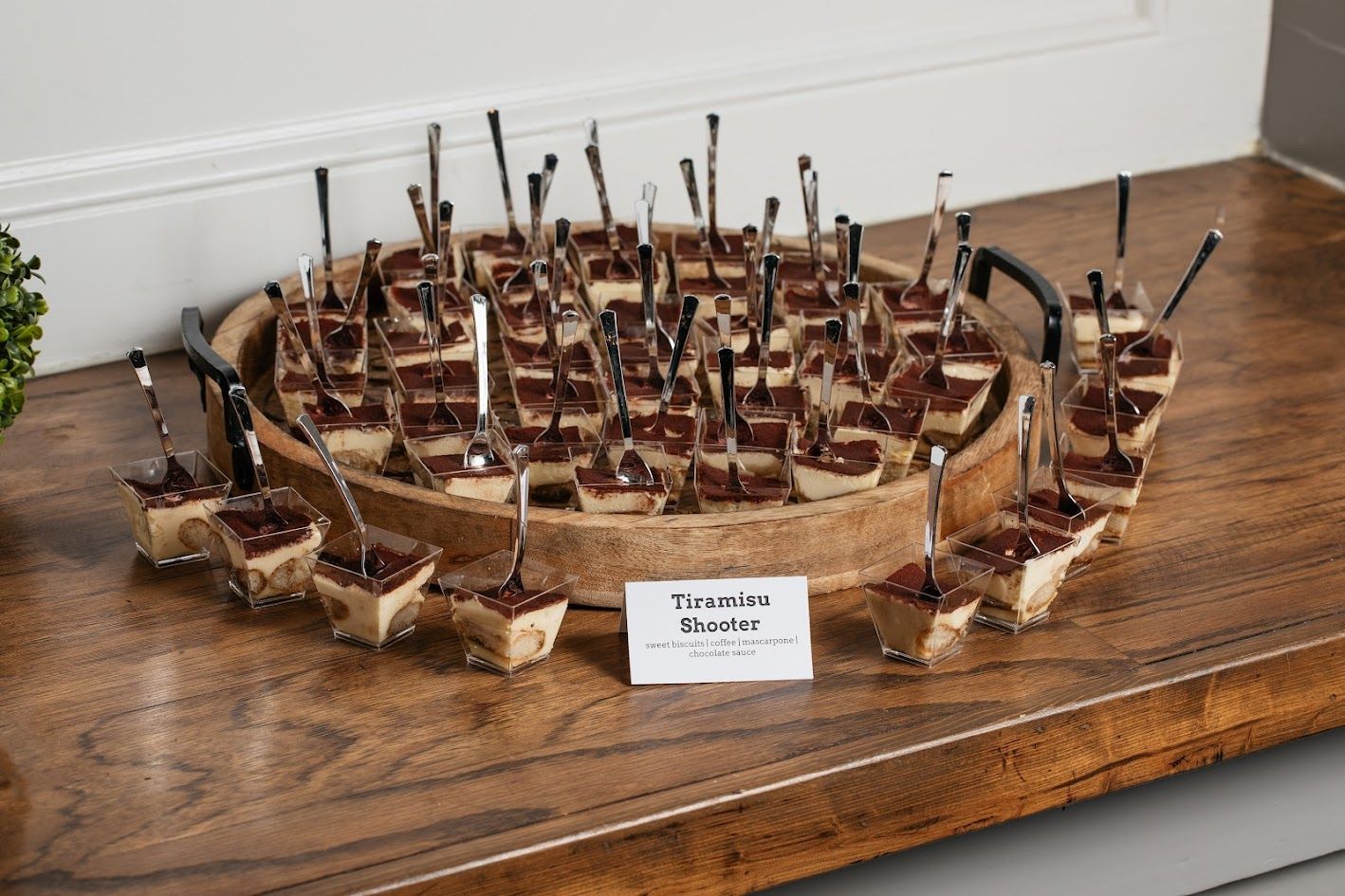 A wooden tray filled with tiramisu desserts on spoons on a wooden table.