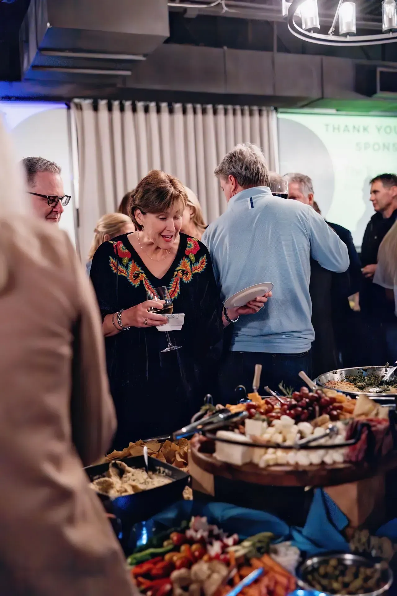 A group of people are standing around a buffet table eating food.