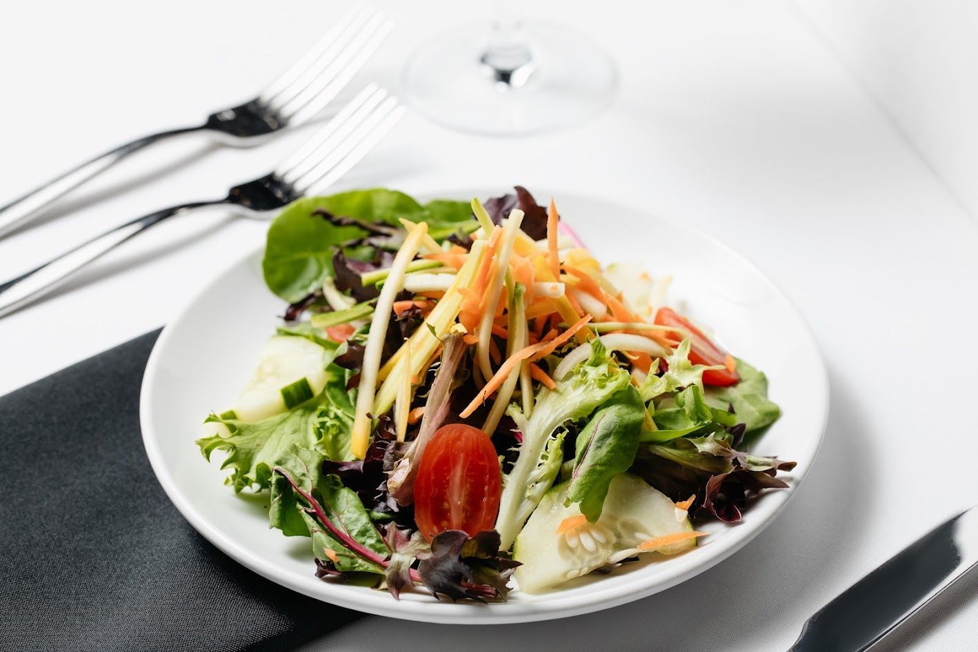 Fresh mixed salad with greens, shredded carrots, and tomatoes on a white plate