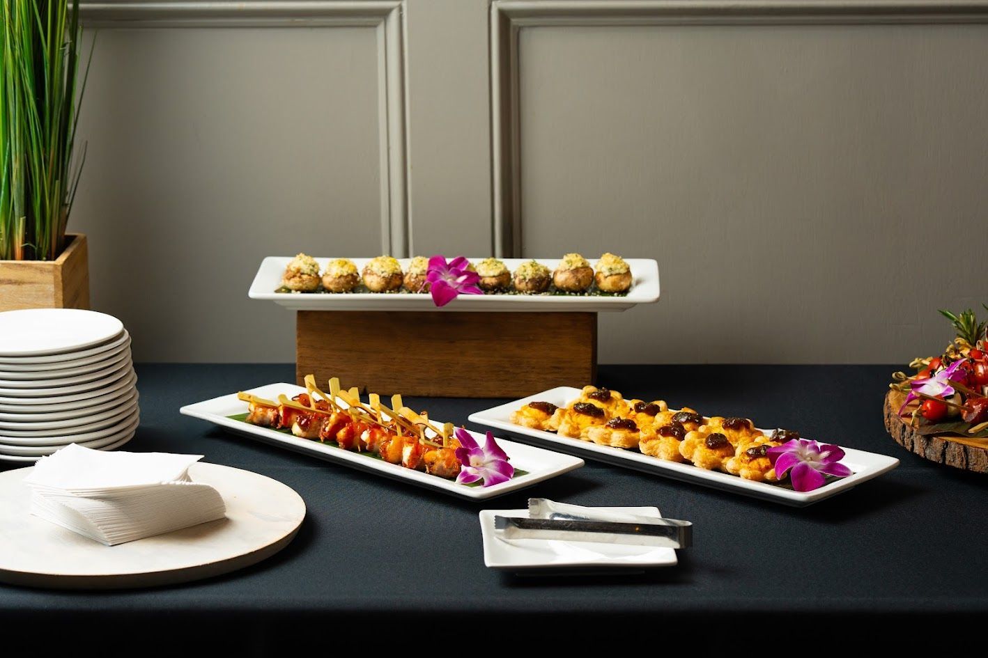 Buffet table with assorted hors d'oeuvres on white platters and plates, styled with flowers and stacked dishes