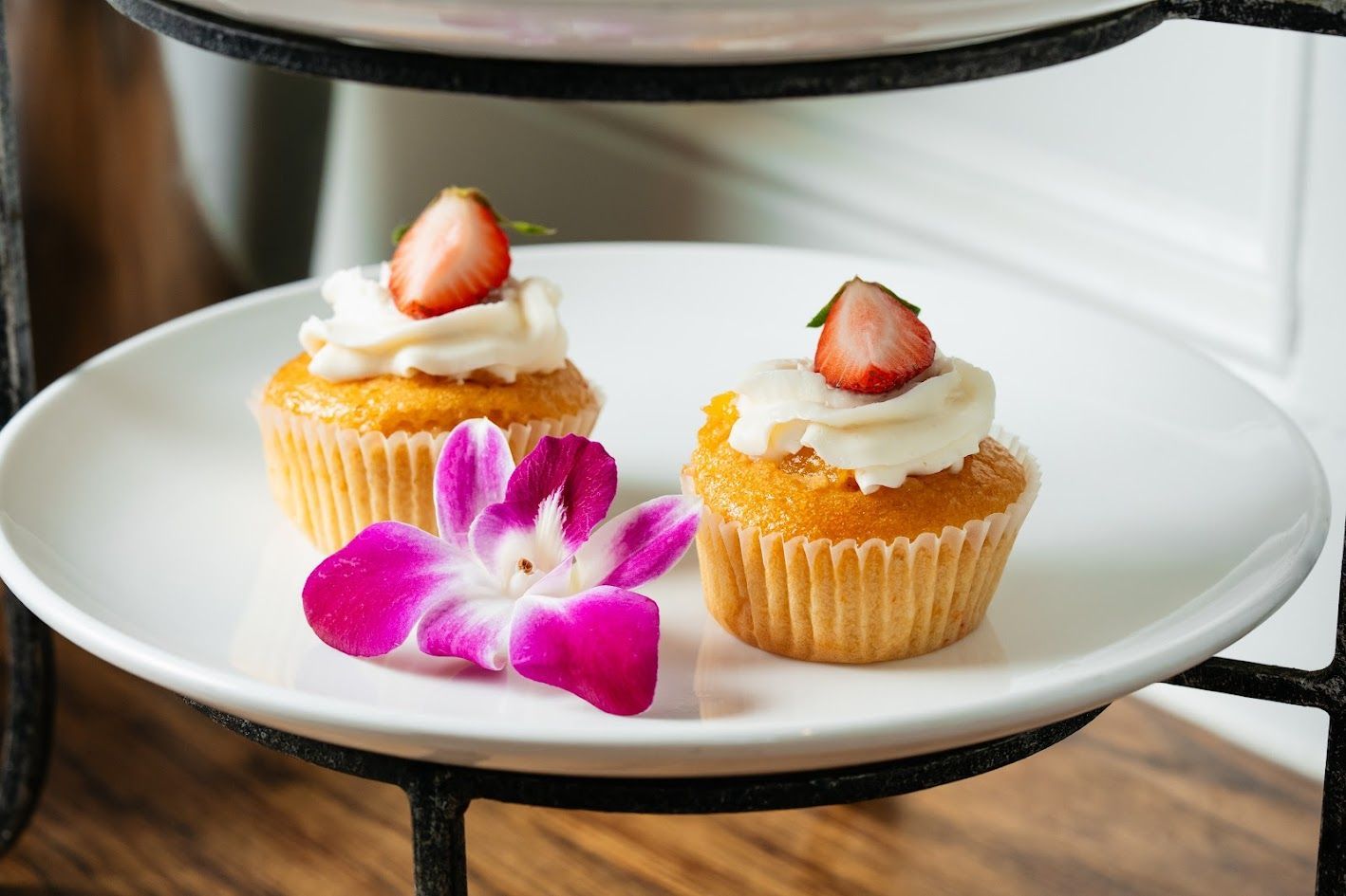 Two strawberry-topped cupcakes on a white plate with a purple orchid garnish
