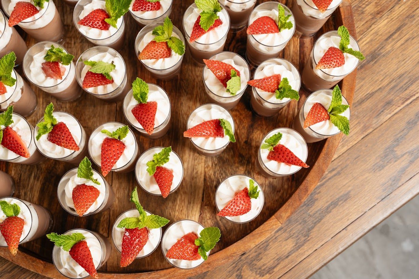Strawberry-topped mini desserts arranged on a wooden tray, viewed from above.