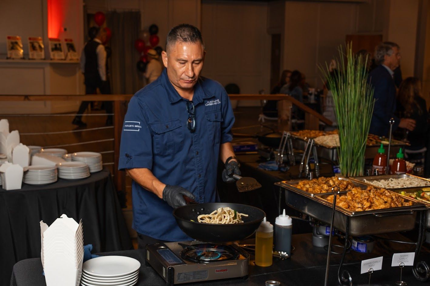 Chef serving food at a buffet with trays, bowls, and tongs in a banquet hall