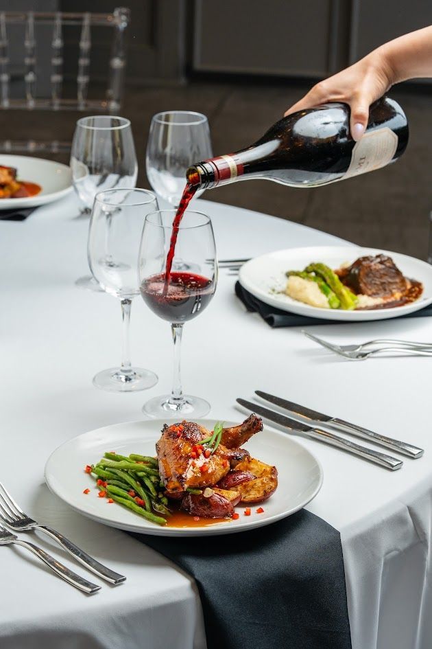 Server pouring red wine into a glass at a fine dining table with plated meals and white tablecloth