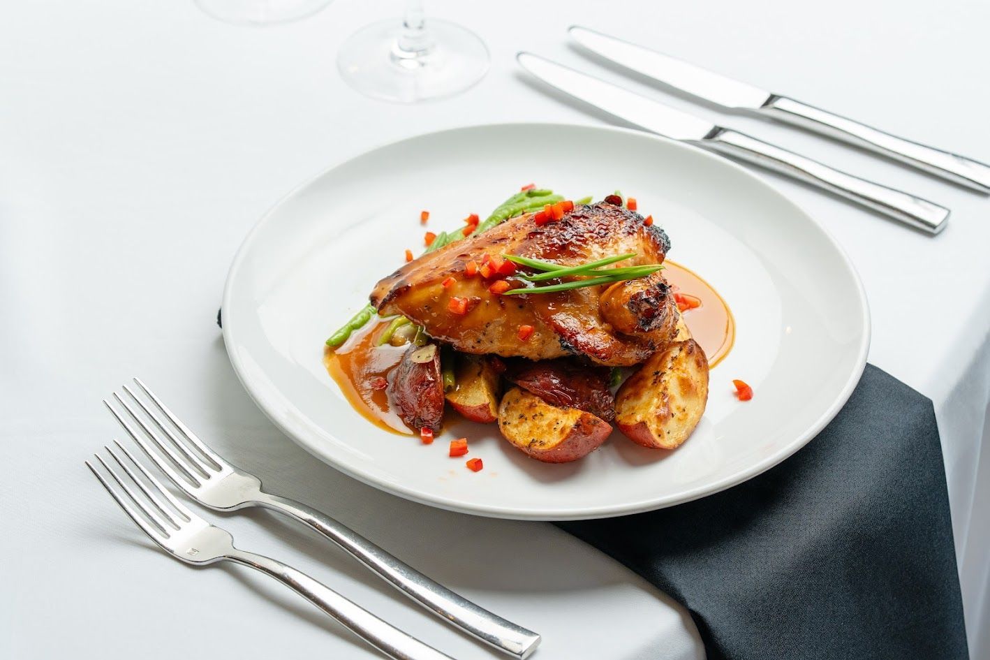 Plated roasted chicken with potatoes and sauce on a white tablecloth, set with silverware