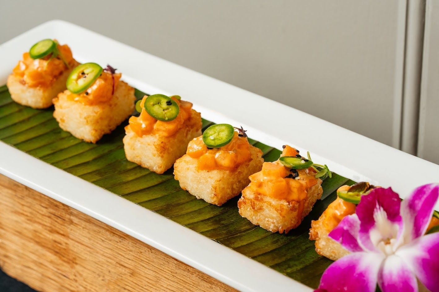 Plated sushi bites topped with jalapeño on a banana leaf, garnished with an orchid