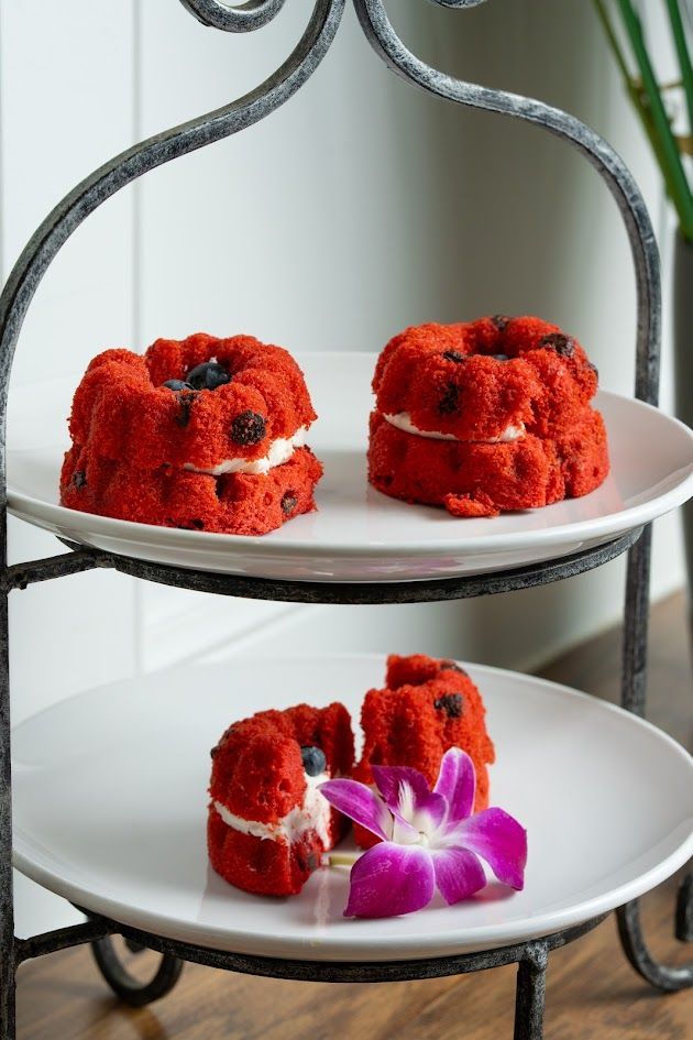 Two red frosted mini cakes on a white tiered stand with a purple orchid garnish